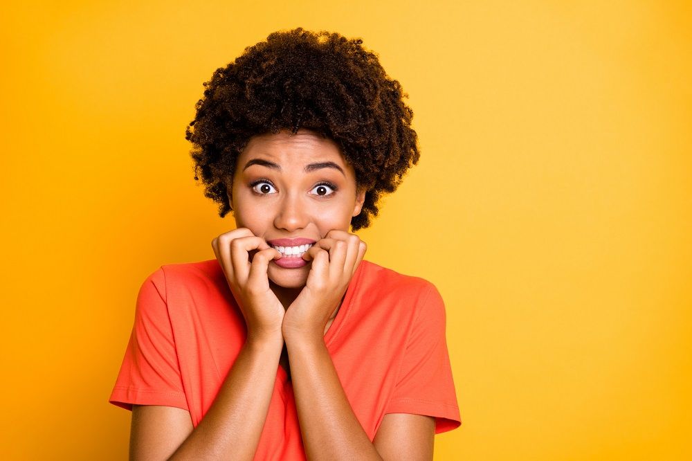 Woman biting her fingernails in fear wearing an orange shirt on a yellow background dental anxiety sedation dentistry dentist in Dallas Texas